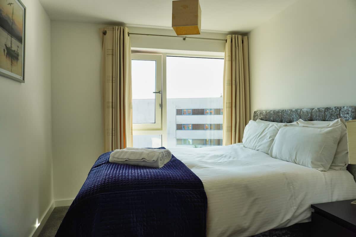 Une chambre d’hôtel avec un lit, une table de chevet, une fenêtre avec des rideaux et une vue sur un bâtiment à l’extérieur.