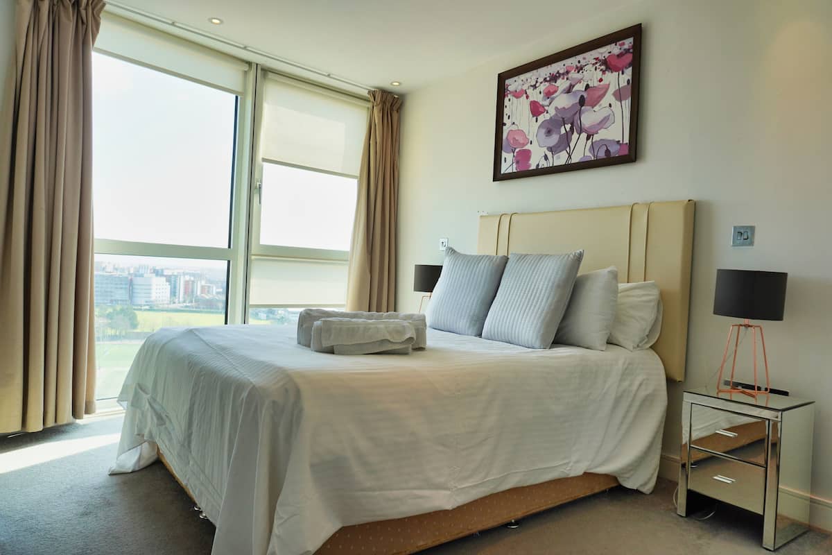 Une chambre d’hôtel avec un grand lit, une table de chevet avec une lampe et une fenêtre avec des rideaux.