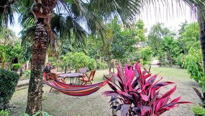 A garden with a hammock, wooden chairs, and a table. - Eden Jungle Resort (Sauraha)