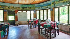 A dining area with tables and chairs, a whiteboard with text, and large windows. - Eden Jungle Resort (Sauraha)