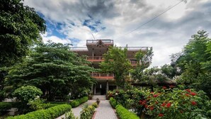 A building with a central entrance, surrounded by lush greenery and a pathway leading to it. - Eden Jungle Resort (Sauraha)