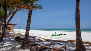 A beach with sun loungers, palm trees, and a clear blue sky. - Blue Marlin Beach Hotel  (Diani Beach)