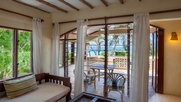 A room with a bed, a table, and a view of the outdoors. - Blue Marlin Beach Hotel  (Diani Beach)
