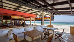 An outdoor seating area with a view of the beach, wooden furniture, and a bar with a Guinness sign. - Blue Marlin Beach Hotel  (Diani Beach)