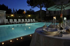 A poolside dining area with a table set for two, surrounded by lounge chairs, and a candle-lit table setting. - Bellariva Feeling Hotel (Rimini)