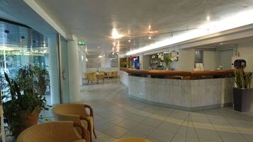 Hall d'albergo con reception, area lounge e piante in vaso.