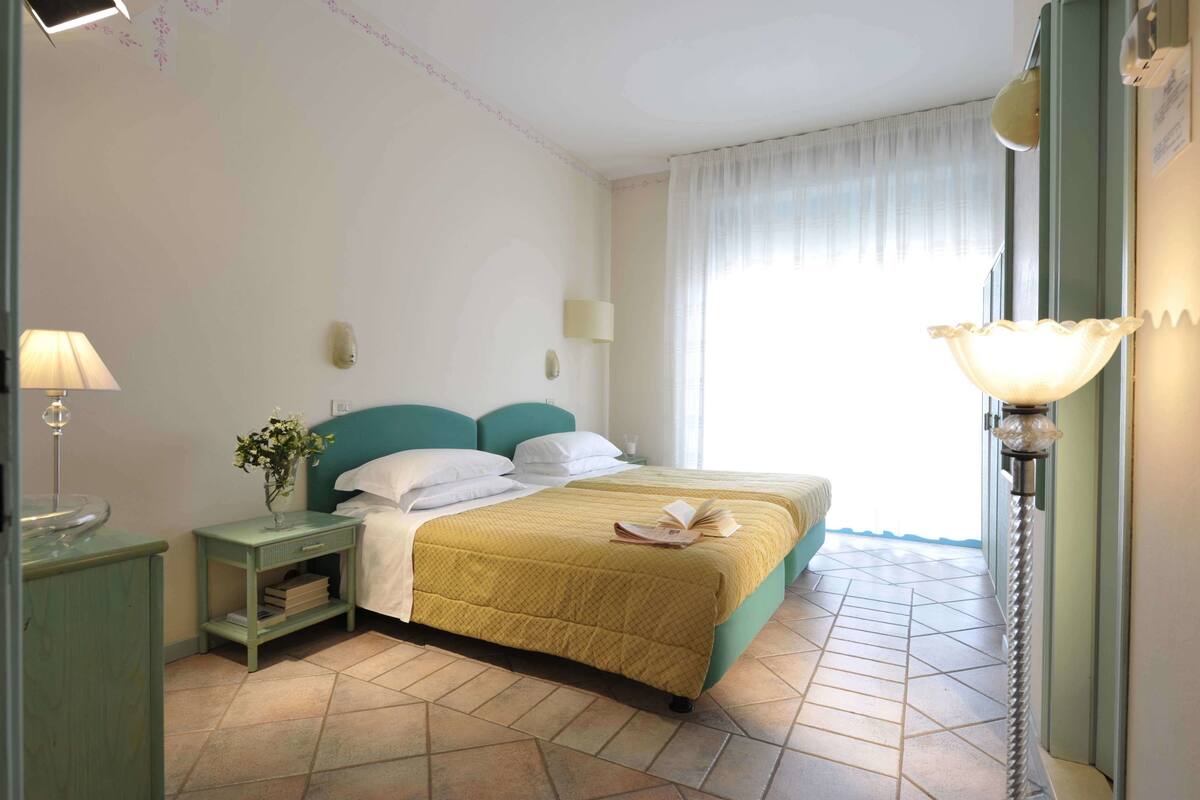 A hotel room with a bed, a nightstand, a lamp, and a window with curtains.
