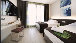A hotel room with two beds, a TV mounted on the wall, a small seating area, and a window with curtains. - Bellariva Feeling Hotel (Rimini)