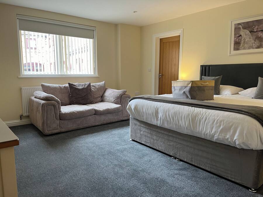 Een slaapkamer met een bed, een bank, een radiator, een raam en een deur.