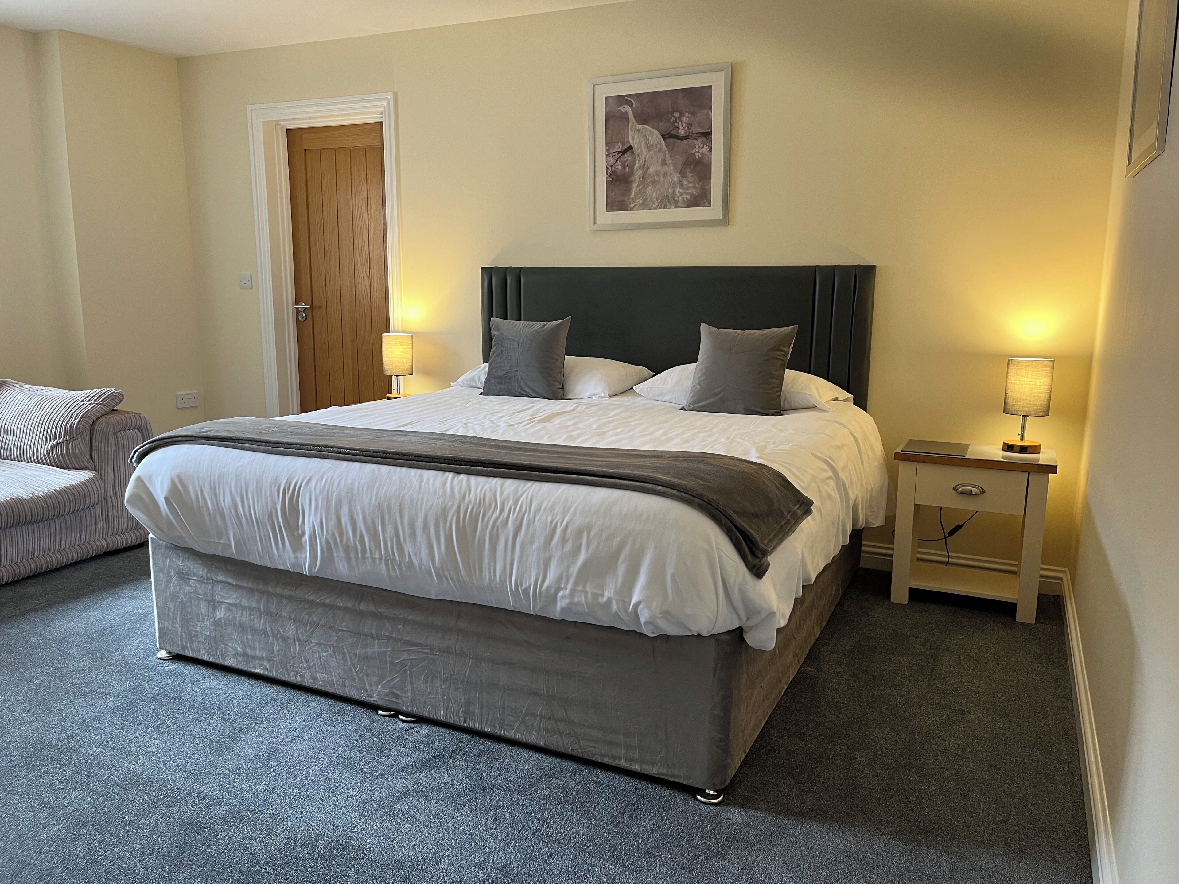 A neatly arranged bedroom with a large bed, bedside lamps, a framed picture on the wall, and a door.