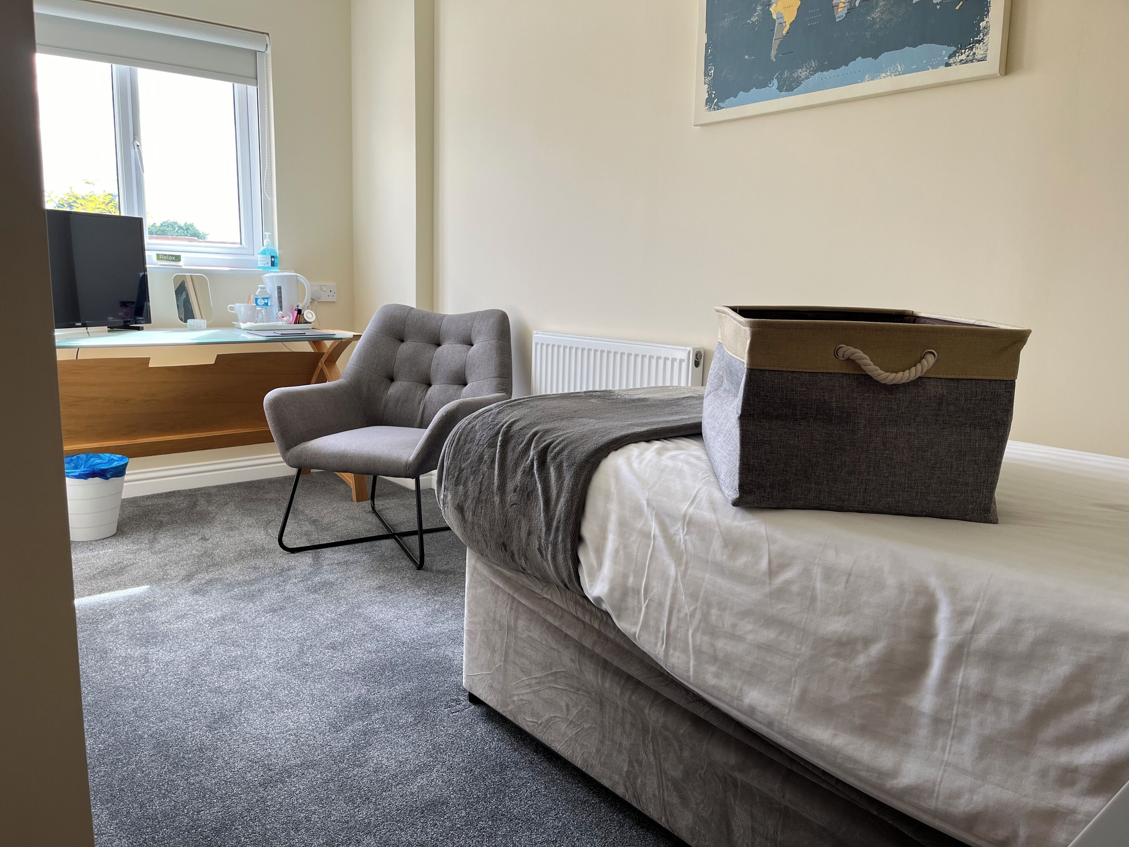 A bedroom with a bed, a grey armchair, a desk with a computer, and a radiator.