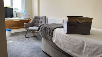 A bedroom with a bed, a grey armchair, a desk with a computer, and a radiator.