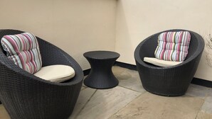 Dos sillones de mimbre con cojines a rayas y una mesita redonda en un patio empedrado.