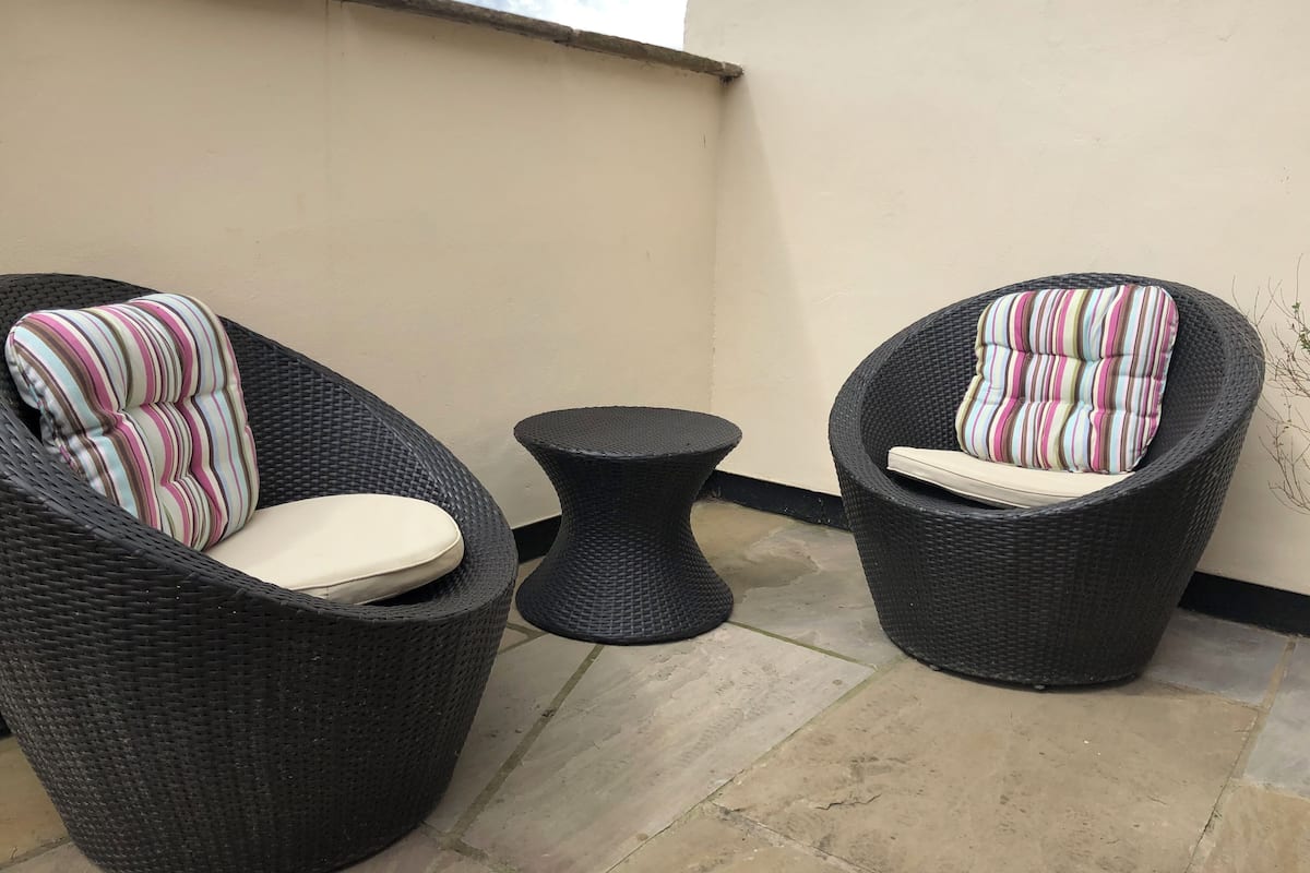 Dos sillones de mimbre con cojines a rayas y una mesita redonda en un patio empedrado.