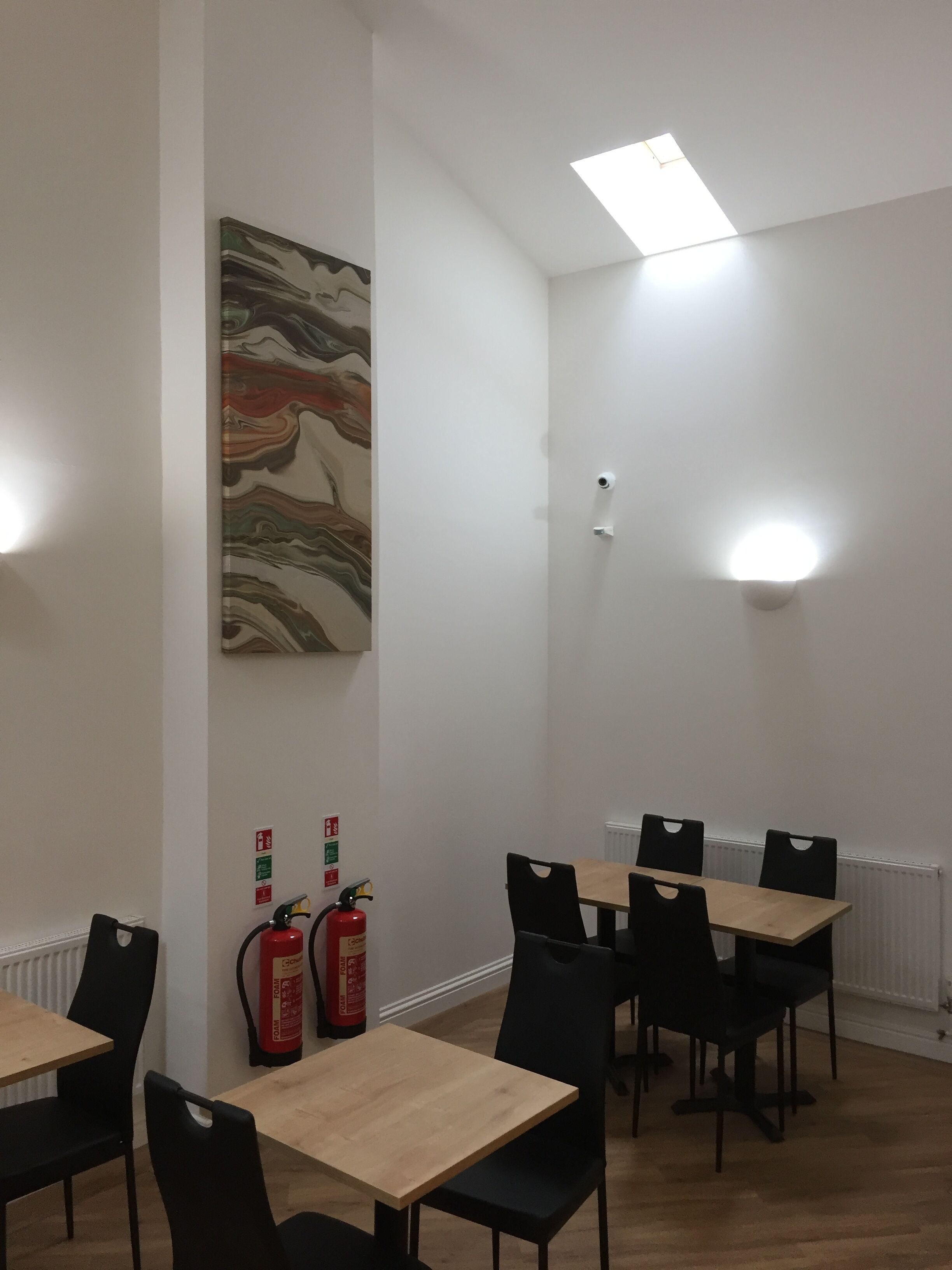A dining area with wooden tables and black chairs, a fire extinguisher, and a ceiling light.