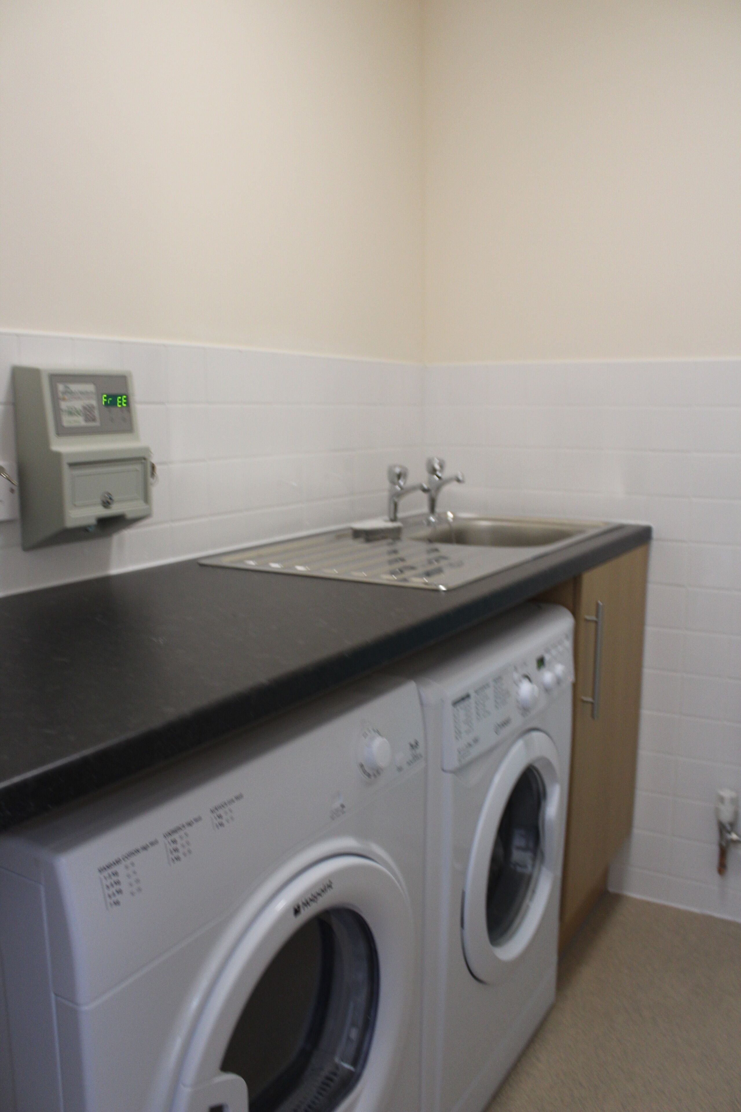 A laundry area with a washing machine and dryer, a sink, and a control panel.