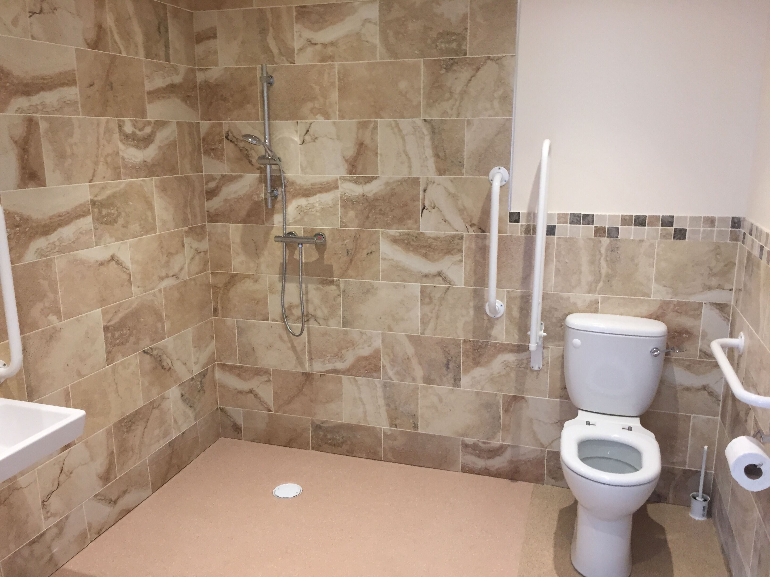 Un baño con ducha, inodoro y barras de apoyo.