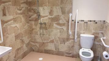 Un baño con ducha, inodoro y barras de apoyo.