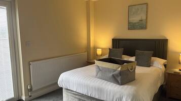 A neatly arranged bedroom with a bed, bedside lamps, a radiator, and a painting on the wall.
