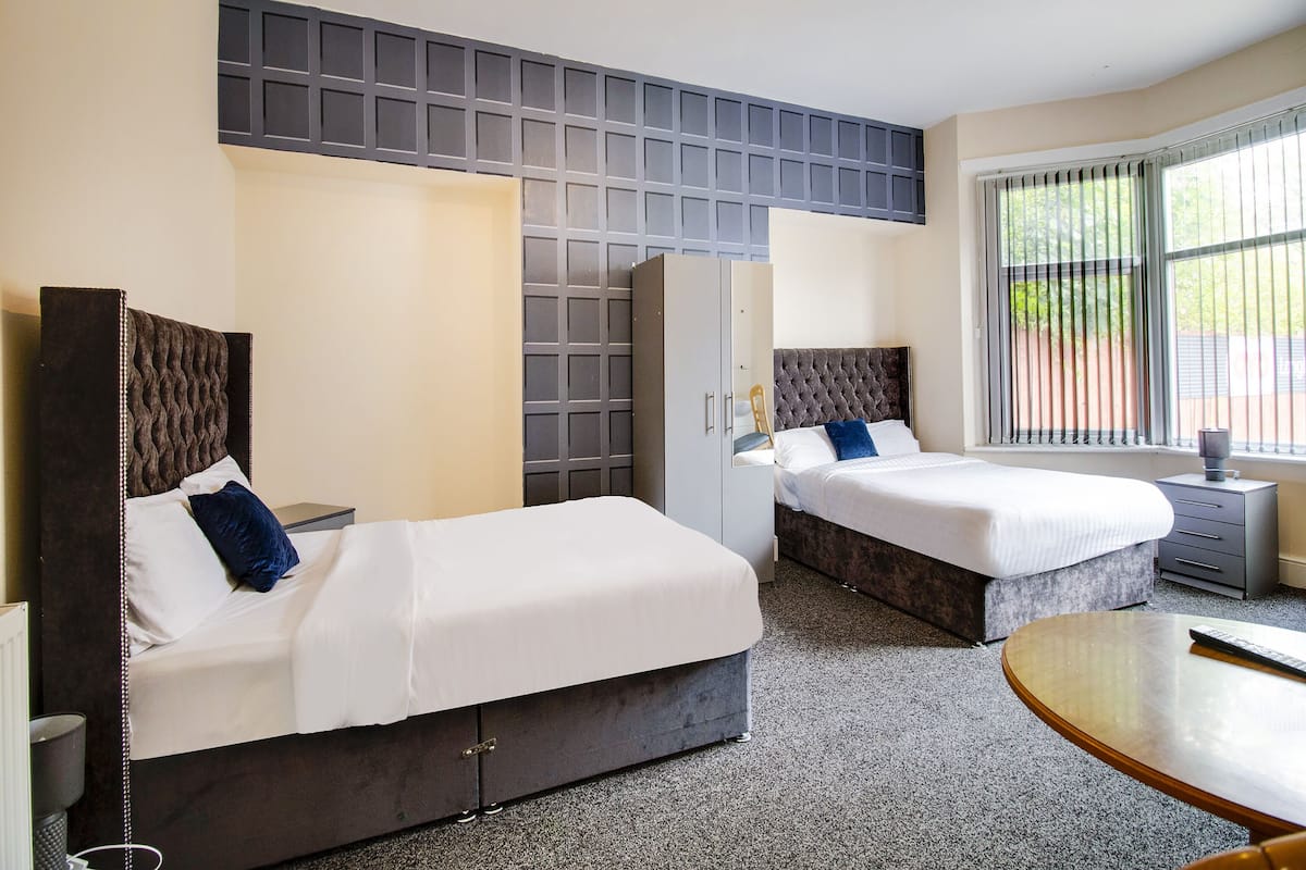 A hotel room with two beds, a wardrobe, a desk, and a window with blinds.