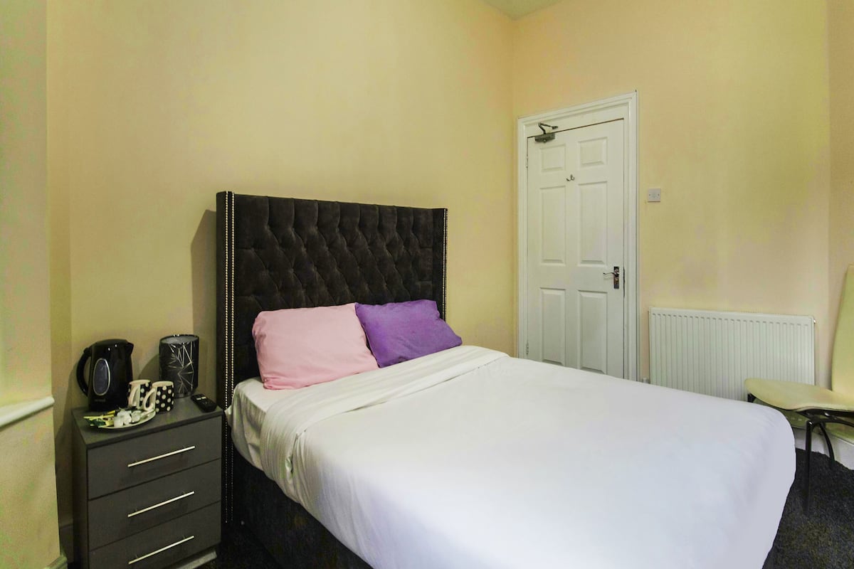 A bedroom with a bed, a dresser, a radiator, and a door.