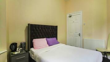 A bedroom with a bed, a dresser, a radiator, and a door.