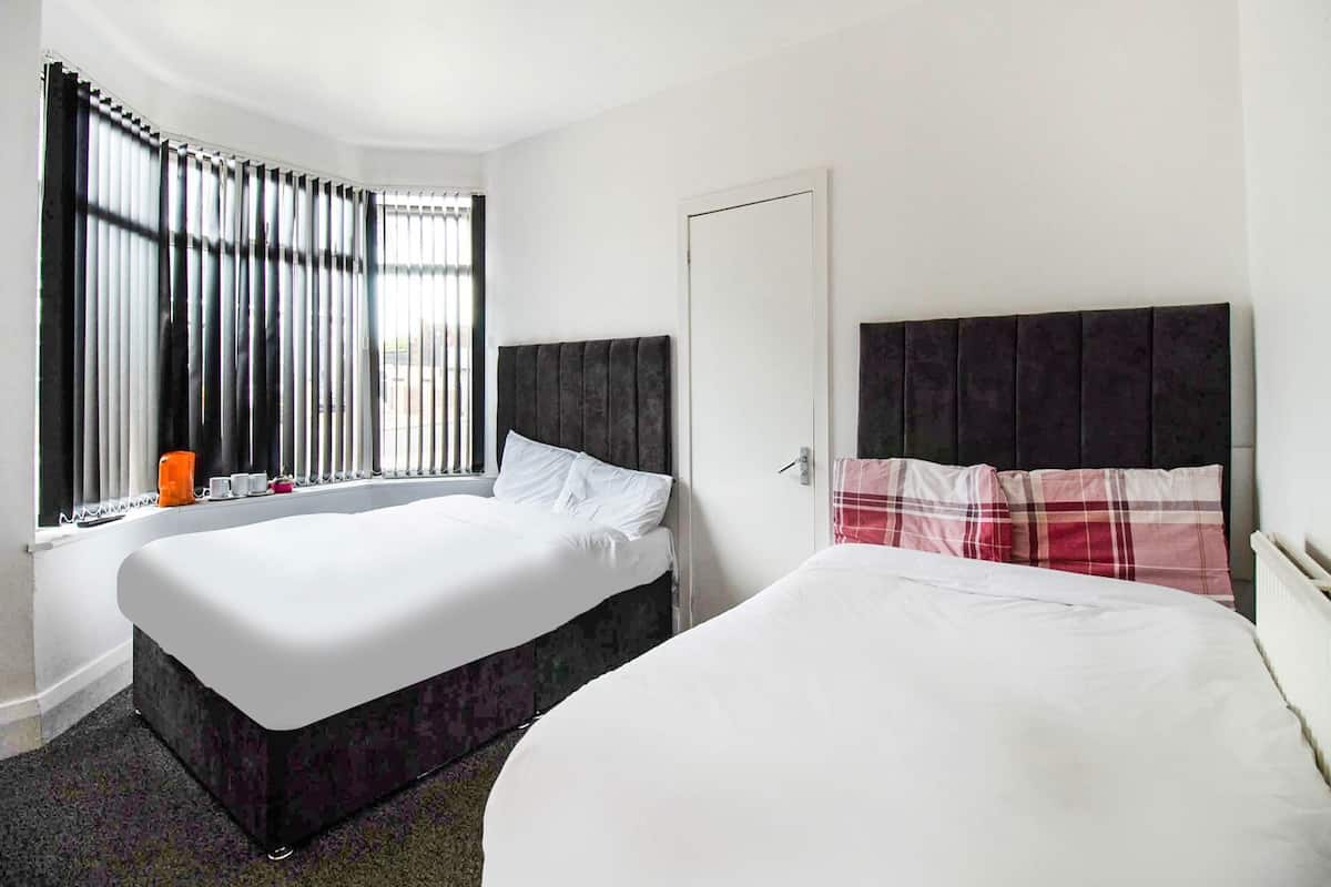 A hotel room with two beds, a window with blinds, a door, and a ceiling light.