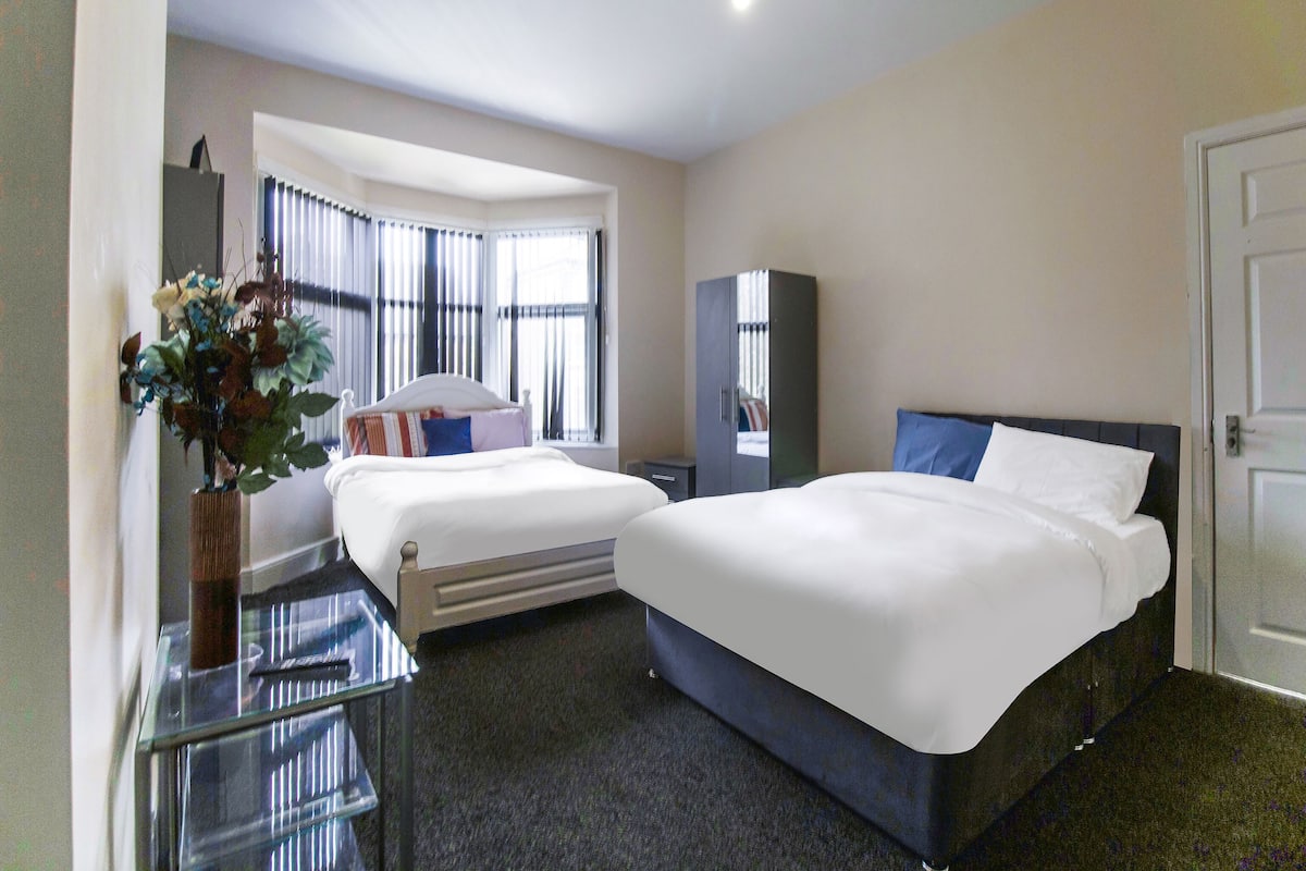 A hotel room with two beds, a desk, and a large window with blinds.