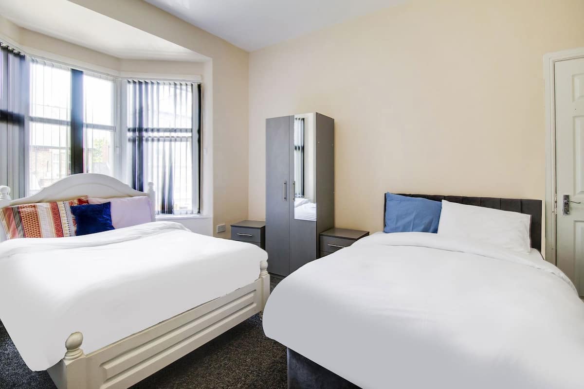 A hotel room with two beds, a wardrobe, a mirror, and a window with curtains.