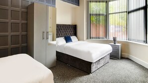 A bedroom with a large bed, a wardrobe, a bedside table, and a window with blinds. - The Longlands Hotel (Middlesbrough)