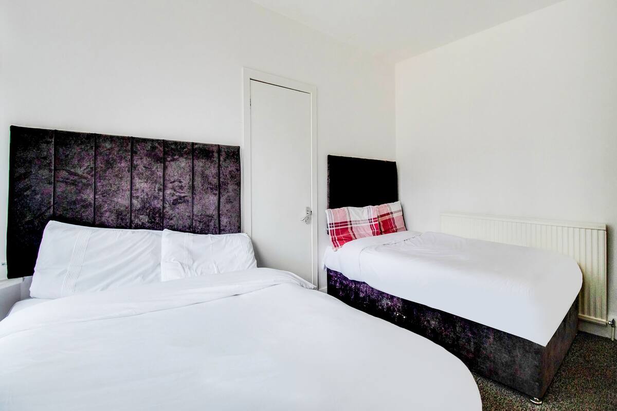 A hotel room with two beds, one with a dark headboard and the other with a white headboard.