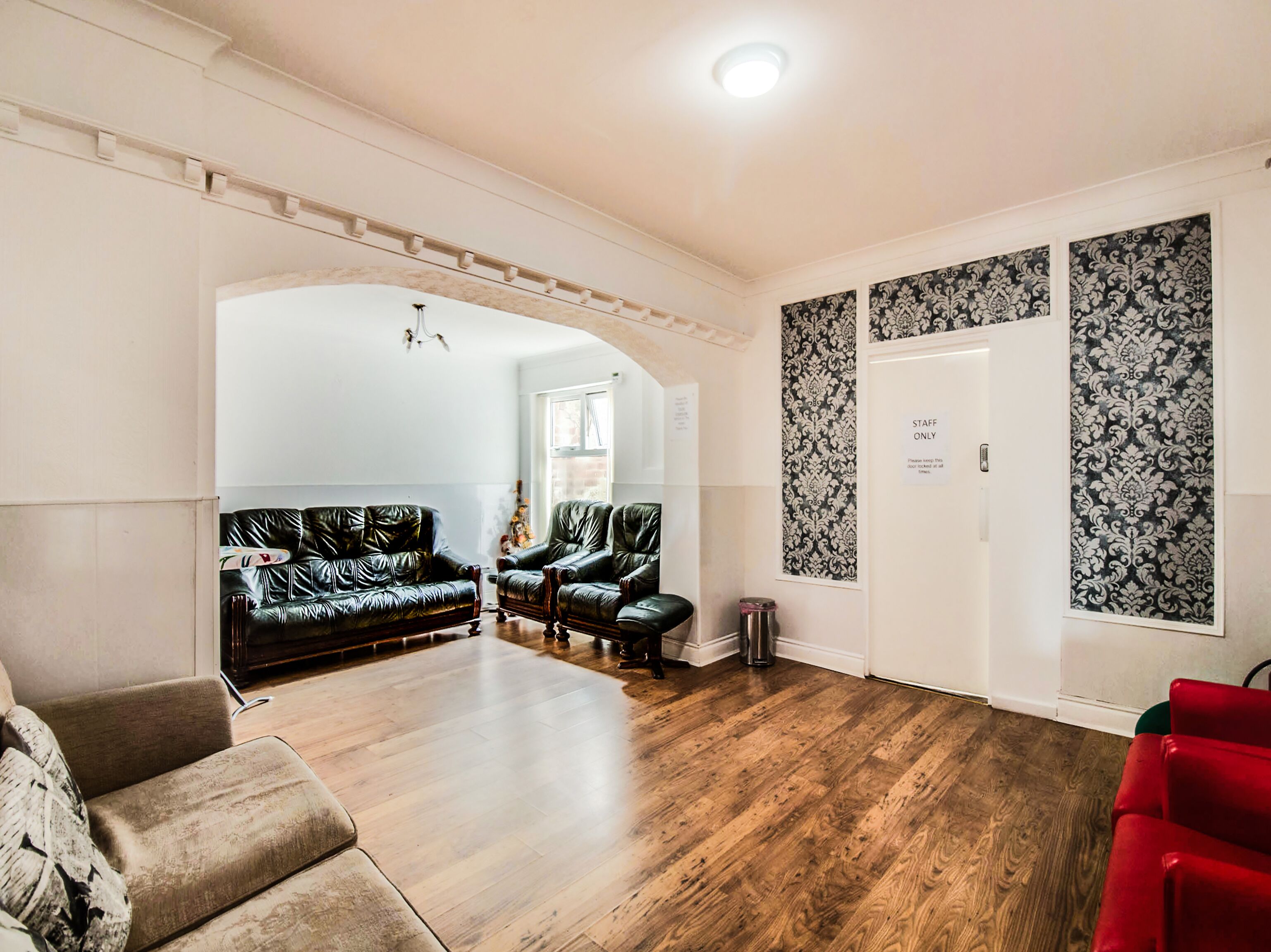 A spacious room with a wooden floor, a black leather sofa, a red chair, and a white door with a 'Staff Only' sign.