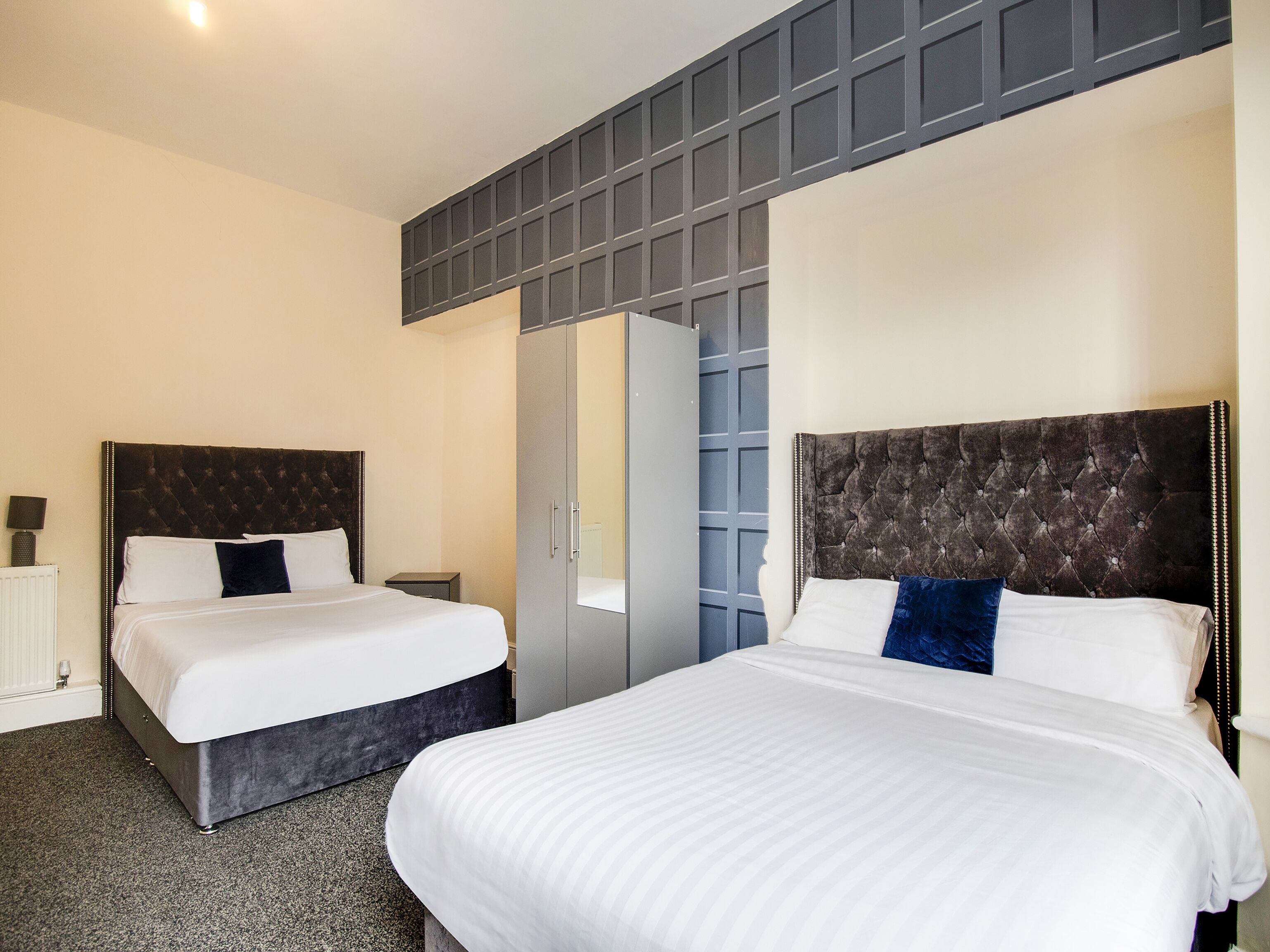 A hotel room with two beds, a wardrobe, and a mirror.