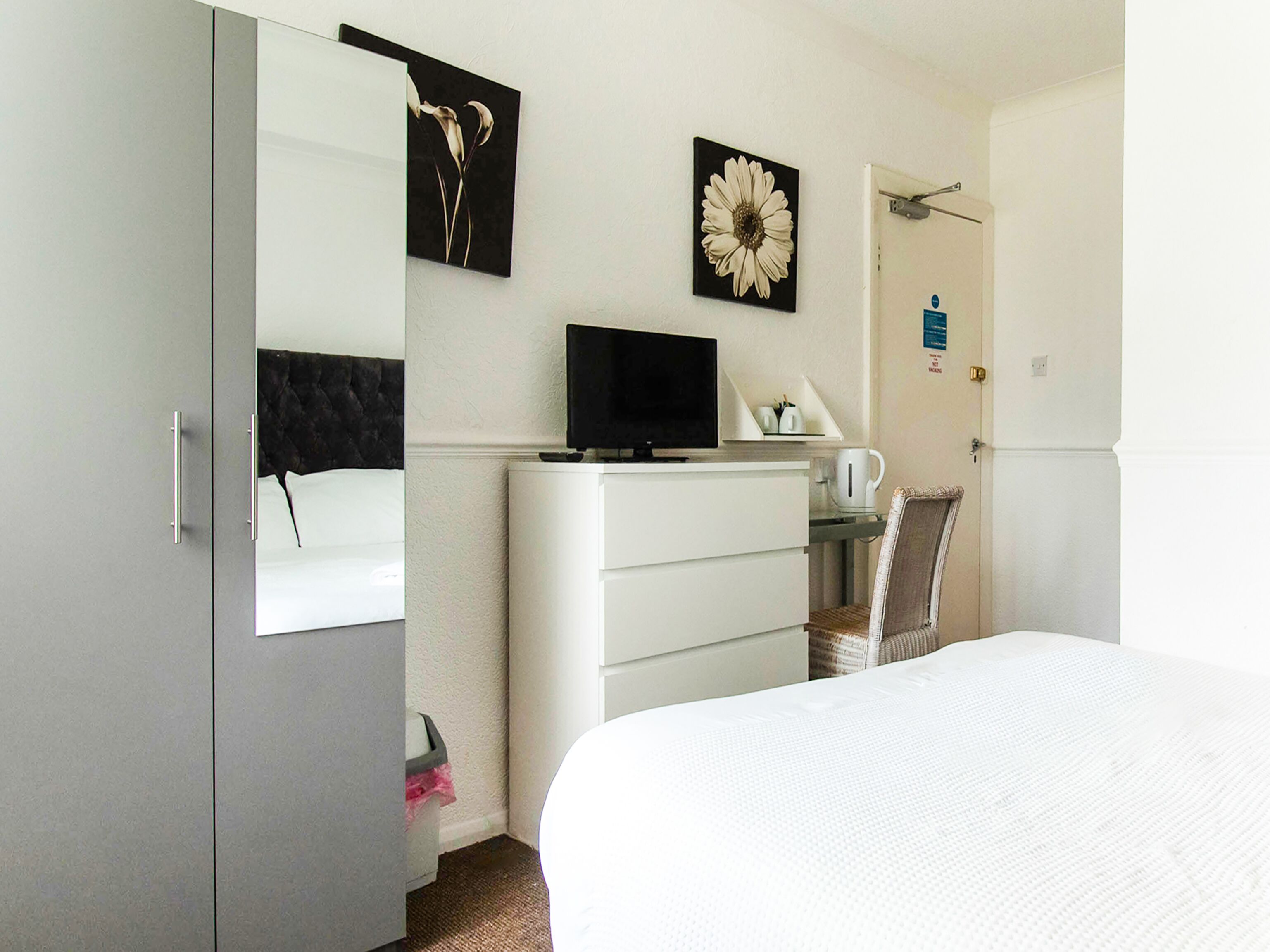 A bedroom with a bed, a desk with a computer, a chair, and artwork on the wall.