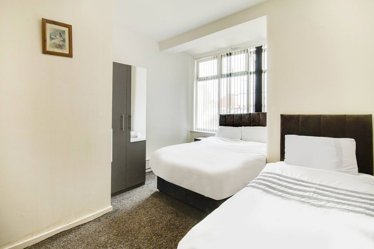 A hotel room with two beds, a wardrobe, a mirror, and a window with curtains.