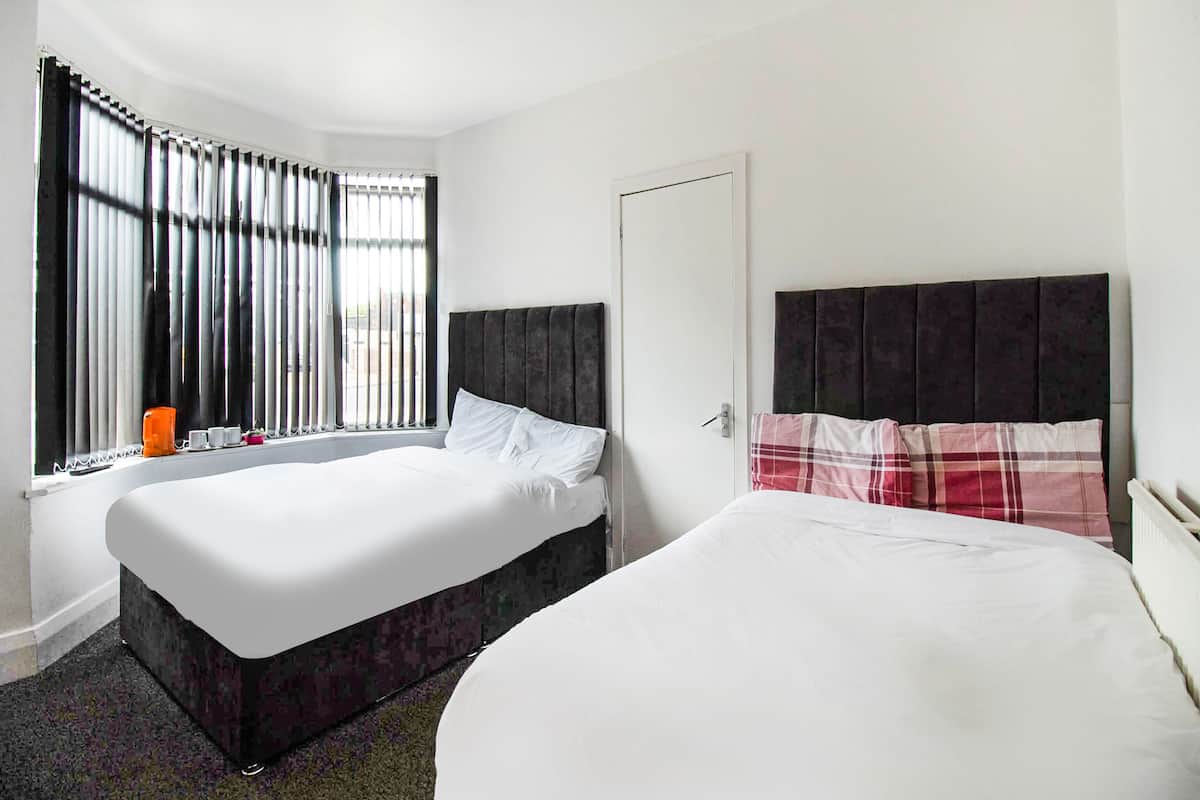 A hotel room with two beds, a window with blinds, a door, and a ceiling light.