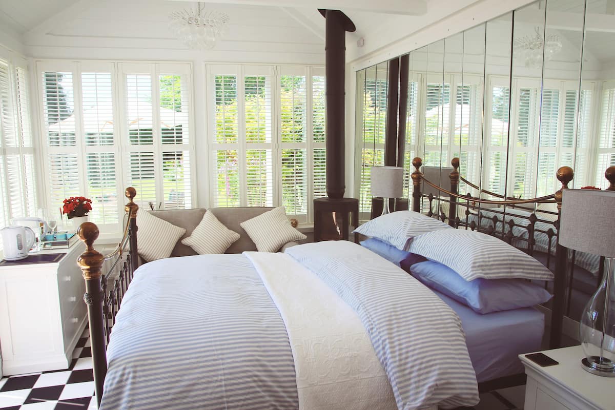 A well-lit bedroom with a large bed, a bedside table, a lamp, and a view through the window.