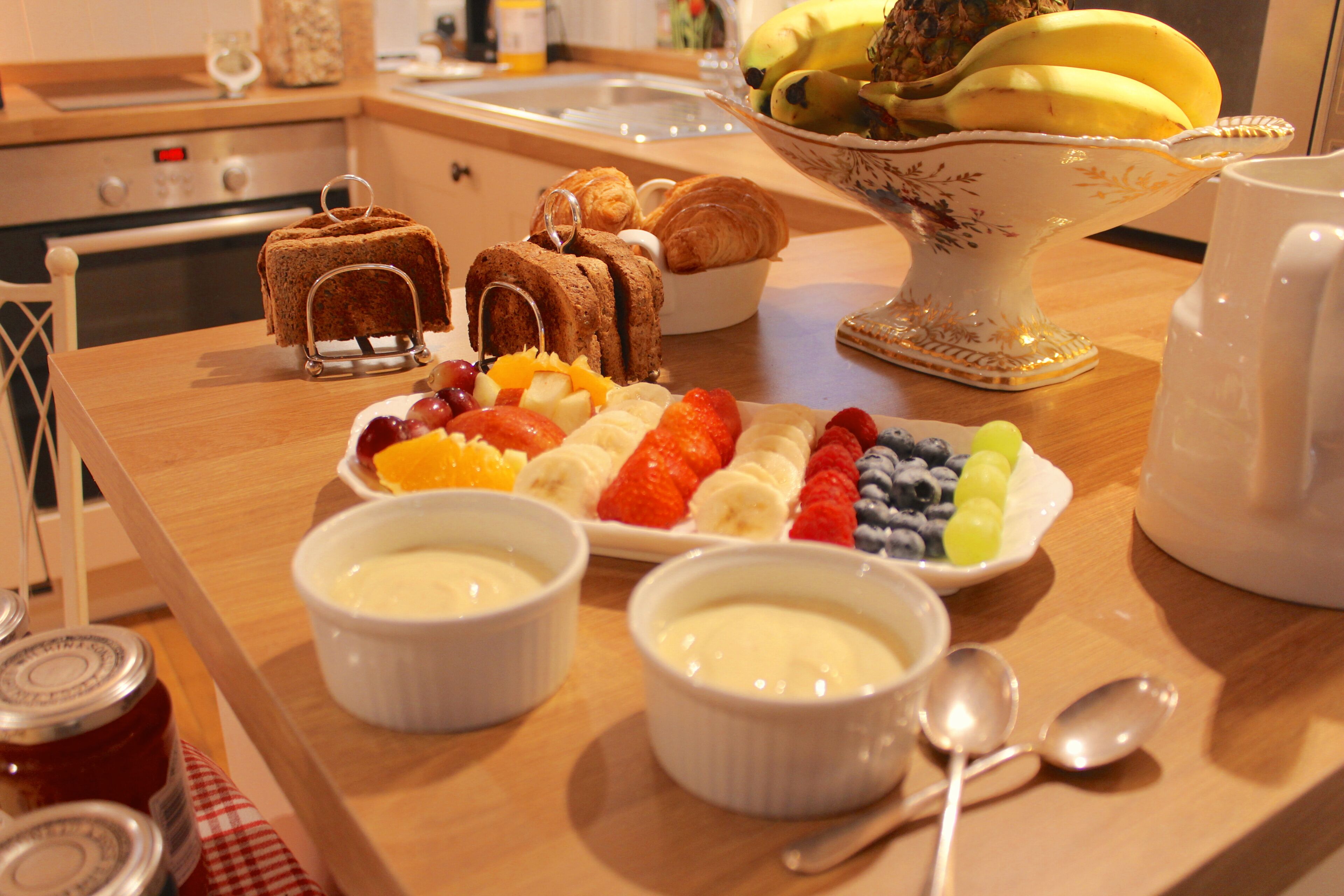 A breakfast buffet with various fruits, pastries, and dairy dishes on a wooden table.