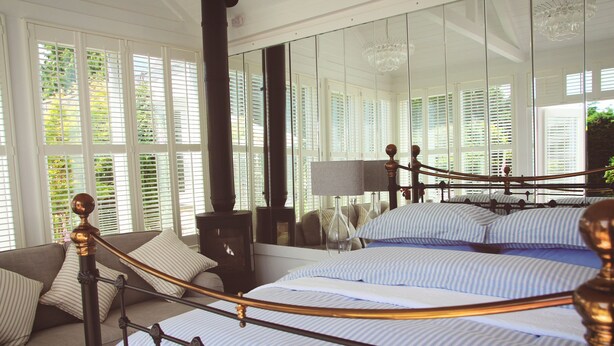 A bedroom with a large bed, a sofa, and a mirror reflecting the room. - Croft House Guest Suite (Stroud)