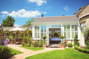Una casa de dos pisos con un jardín cuidado, un patio con muebles de exterior y un cielo azul despejado.