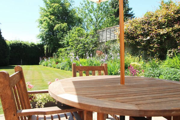 Une table et des chaises en bois, dans un jardin agrémenté de diverses plantes et fleurs.
