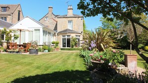 A well-maintained garden with a lawn, potted plants, and a patio area with outdoor furniture. - Croft House Guest Suite (Stroud)