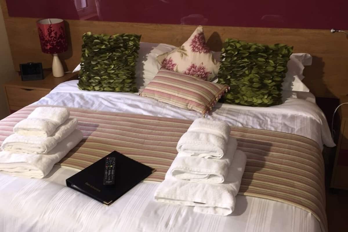 A neatly made bed with folded towels, a remote control, and decorative pillows.