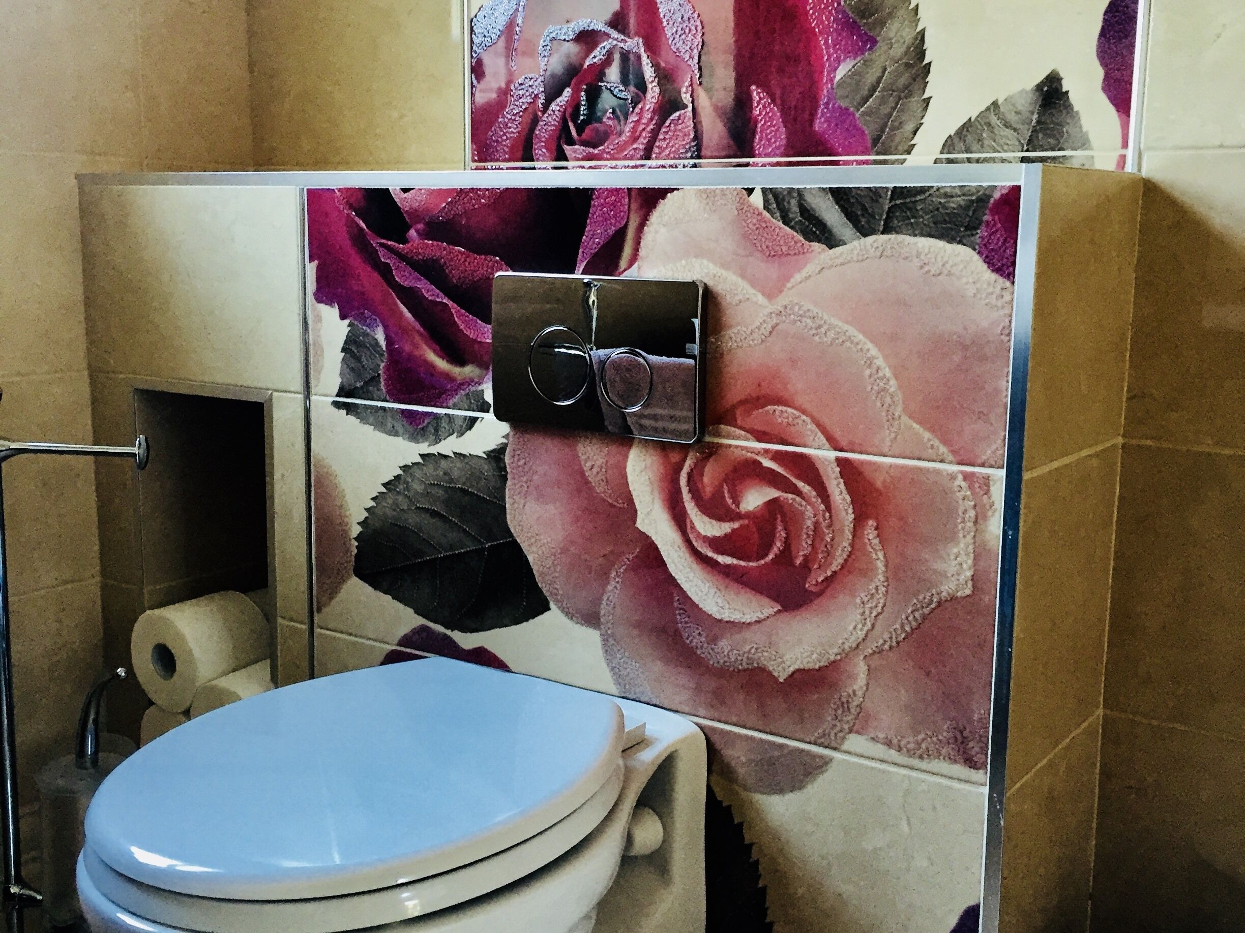 A bathroom with a toilet, a shower, and a wall with floral tiles.