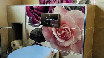 A bathroom with a toilet, a shower, and a wall with floral tiles.
