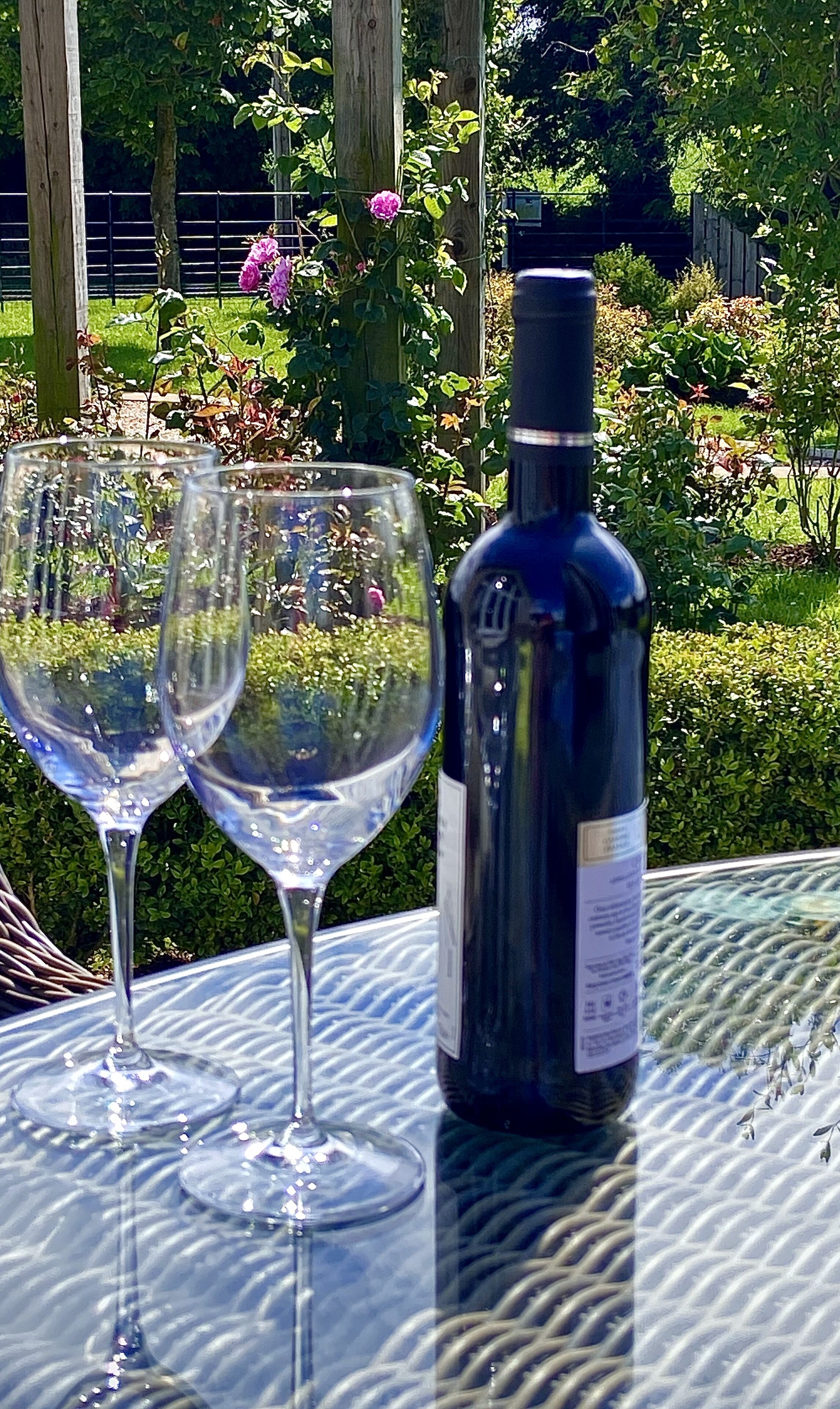 Deux verres à vin et une bouteille sont posés sur une table à l’extérieur.