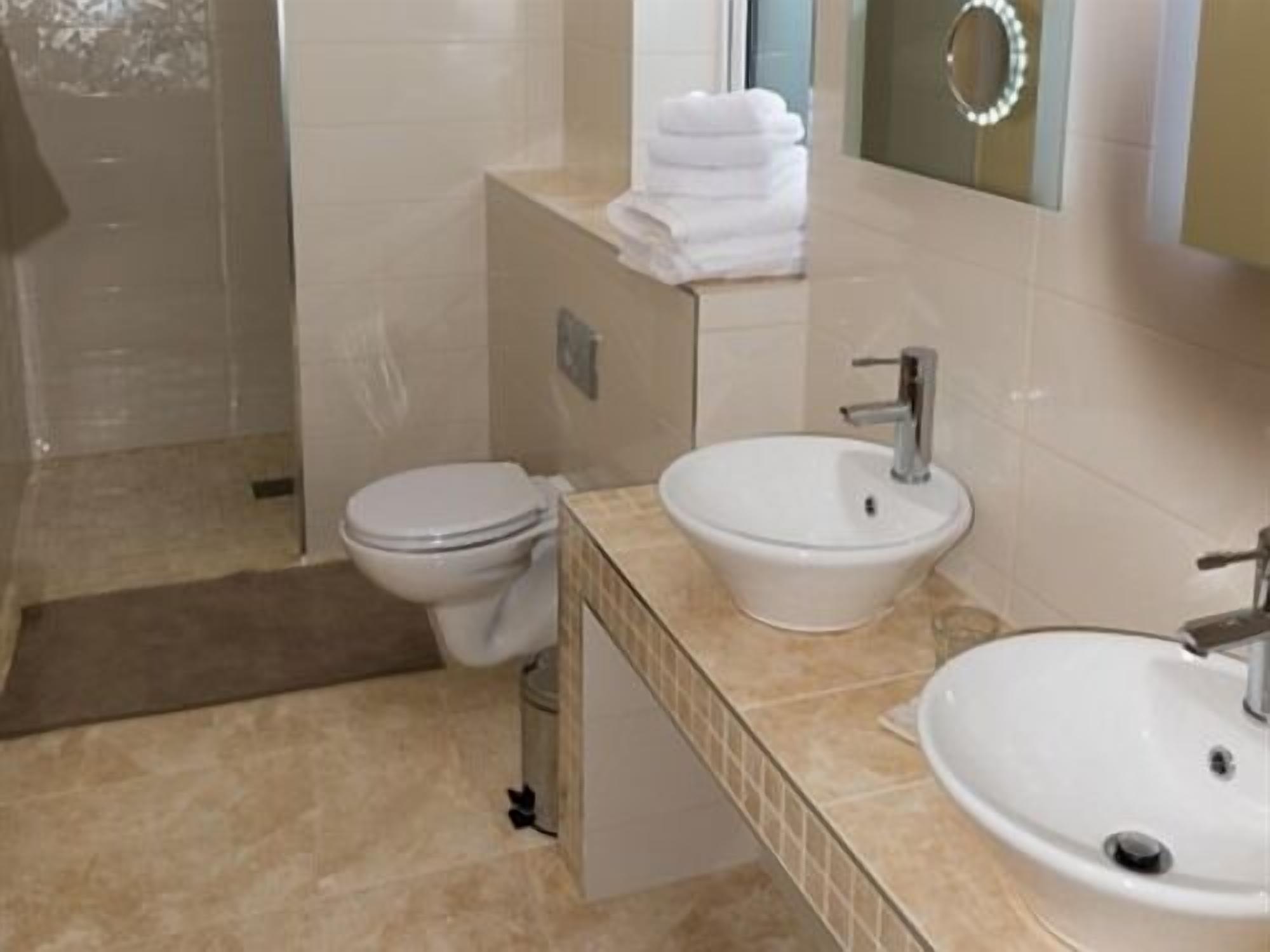 A bathroom with a toilet, two sinks, and a mirror with lights.