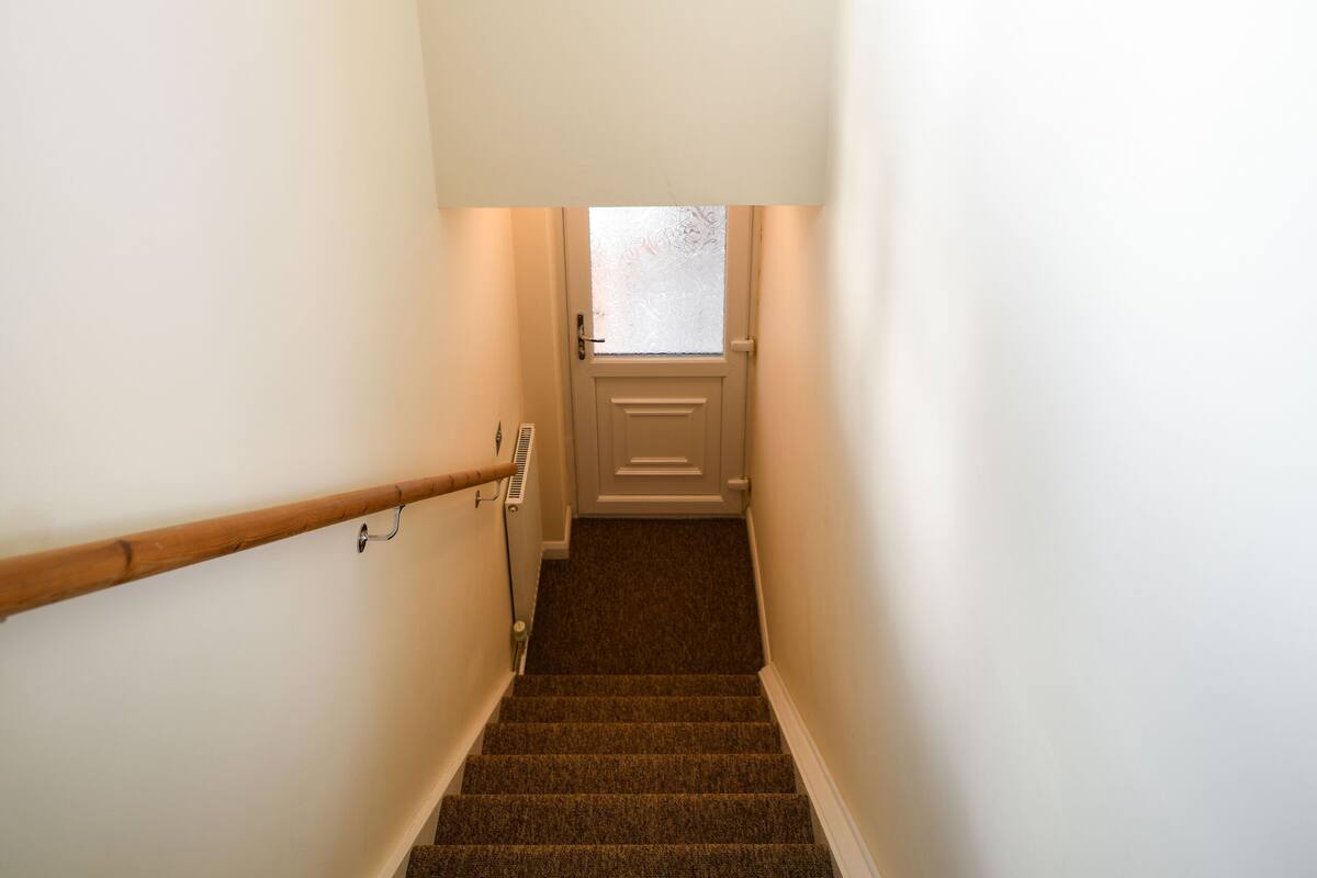 A staircase with a handrail, carpeted steps, and a door at the top.