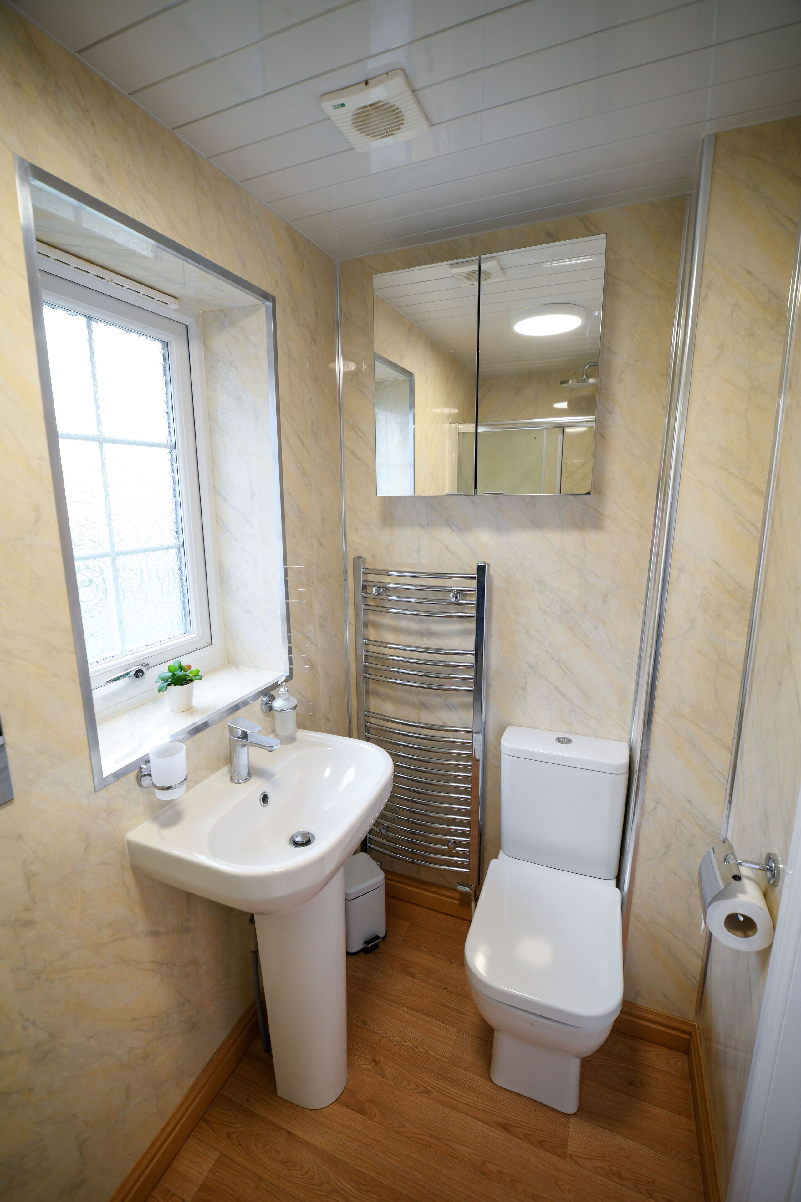 Un baño con lavamanos blanco, inodoro, espejo y ventana.