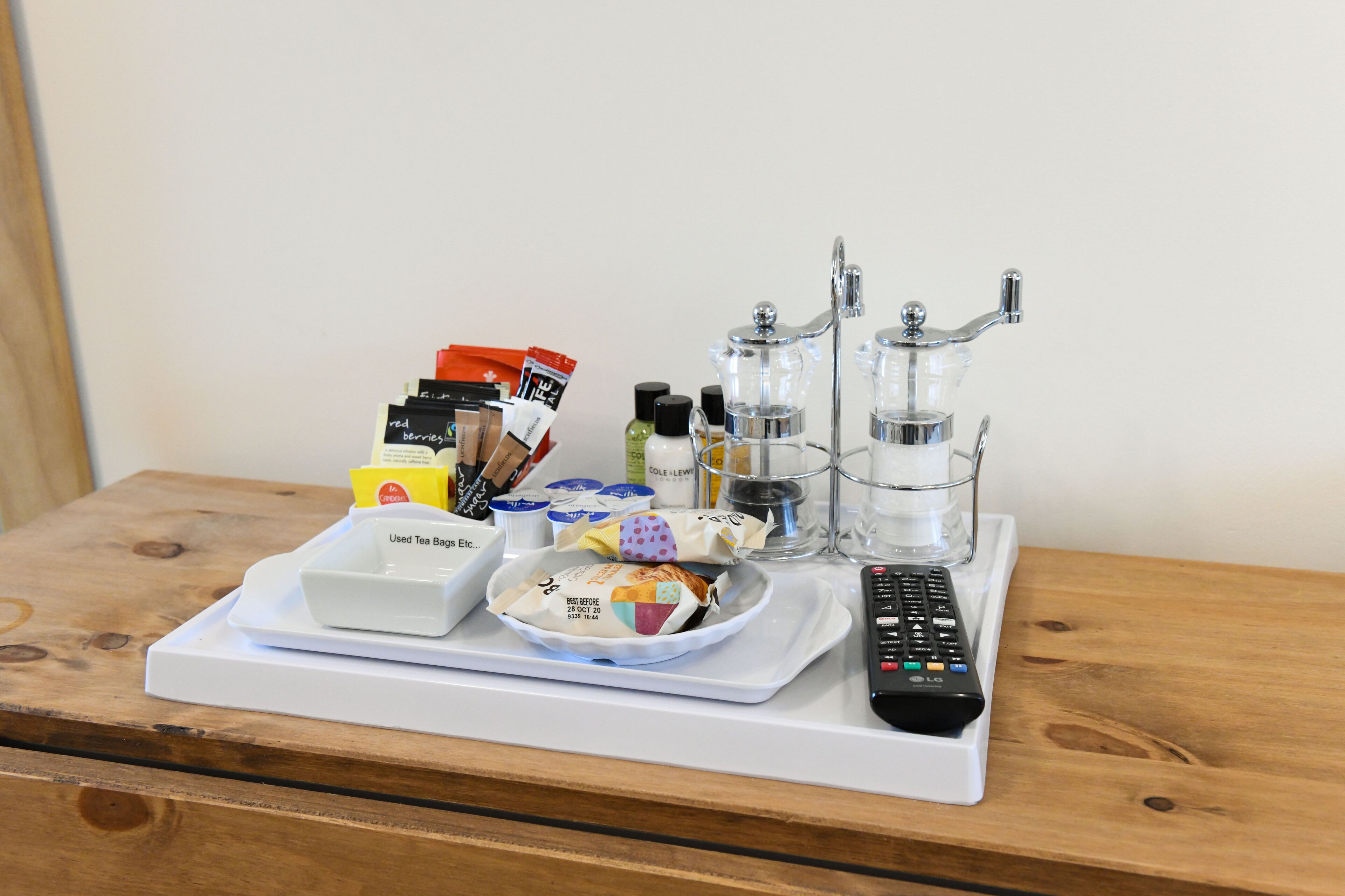 A tray with a remote control, tea bags, and a glass container on a wooden table.